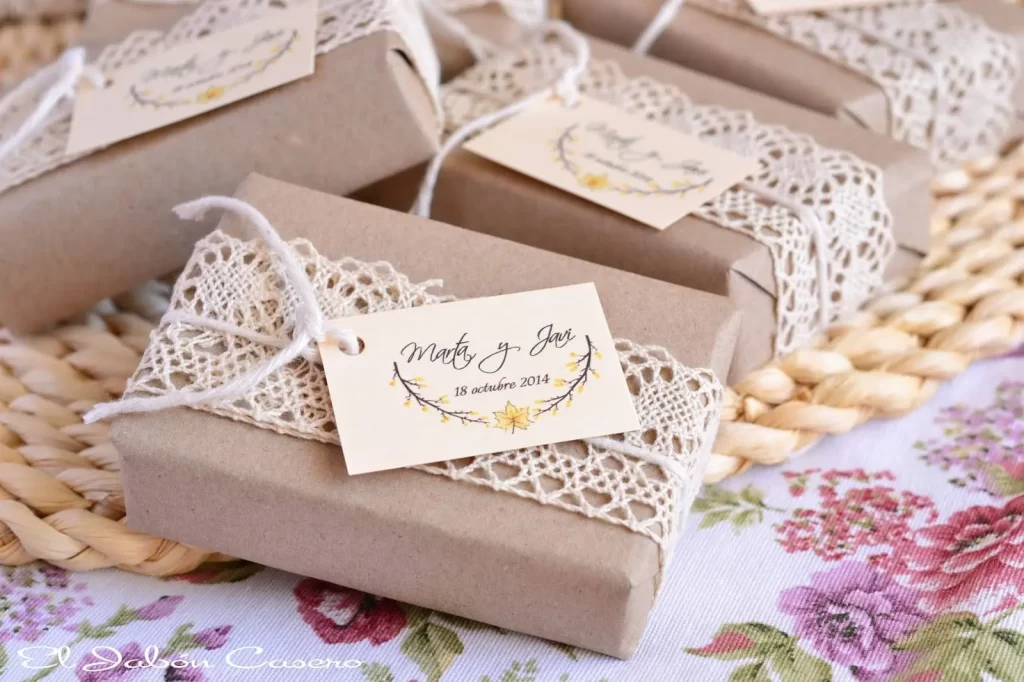 In questa foto scatoline per bomboniere di un matrimonio Shabby Chic chiuse da un nastro di pizzo e il biglietto con nome degli sposi e data delle nozze