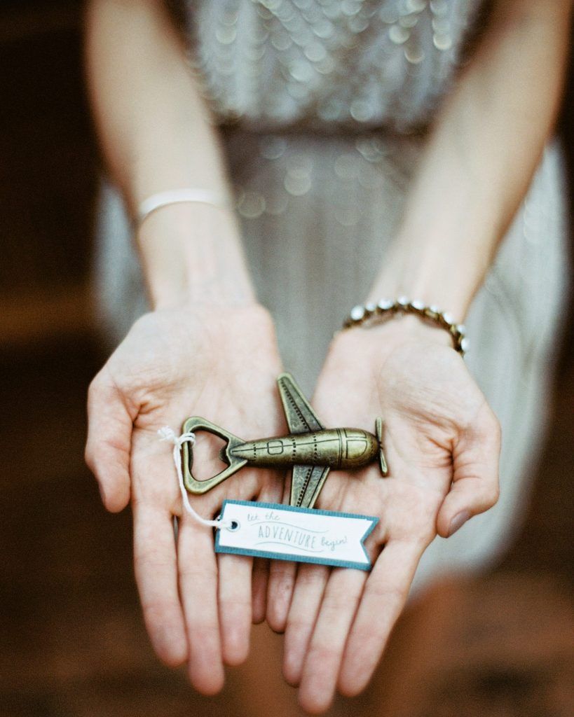 In questa foto una sposa mostra sulle mani la sua bomboniera di matrimonio a tema viaggio a forma di aeroplano colore bronzo con attaccato un biglietto