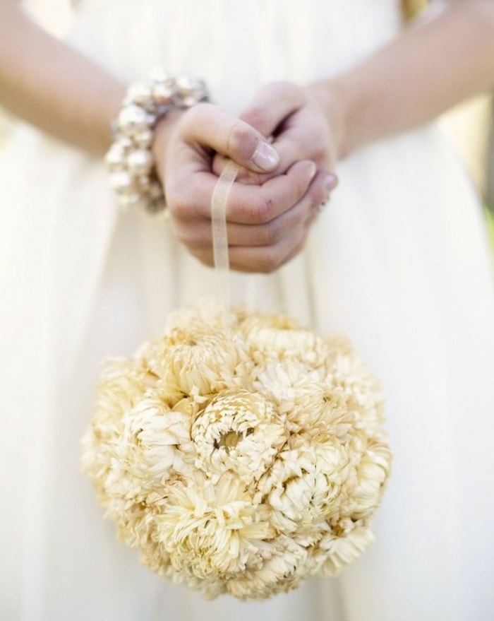 In questa foto le mani di una sposa che tiene un bouquet a borsetta di forma sferica con fiori bianchi legati con un nastro di organza bianca