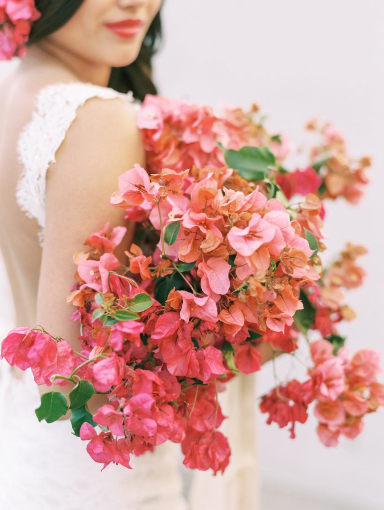 In questa foto una sposa tiene sul braccio destro un ampio bouquet a braccio di buganvillea rosa