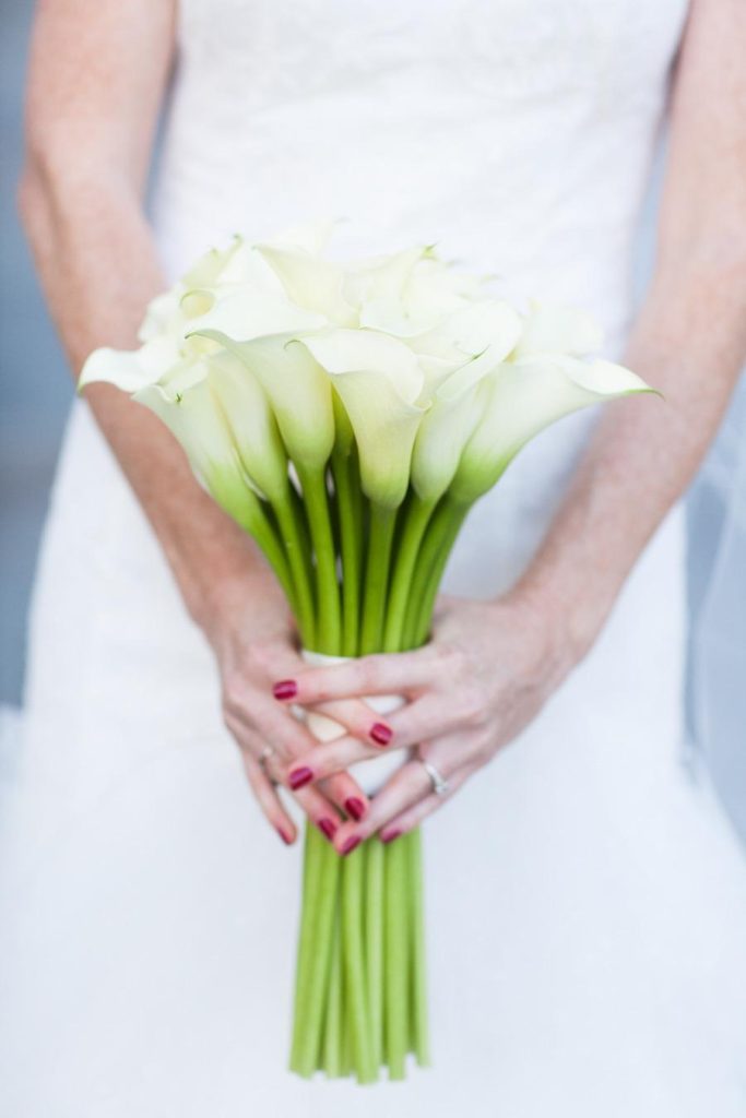In questa foto le mani di una sposa che tiene un bouquet di calle