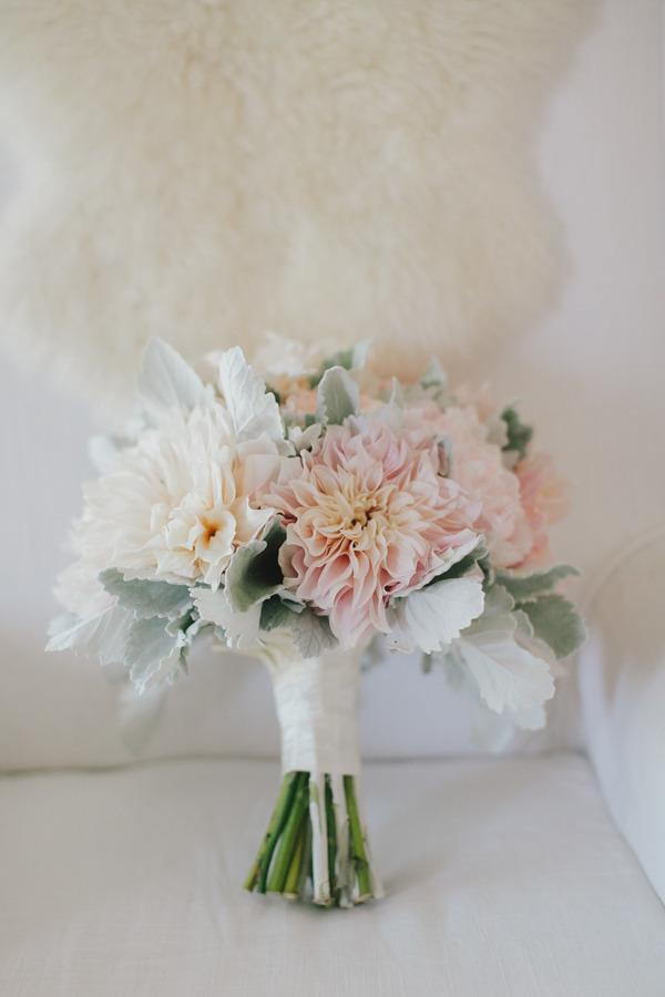 In questa foto un bouquet da sposa di dalie rosa e bianche con legate da un nastro bianco poggiato su una poltrona bianca