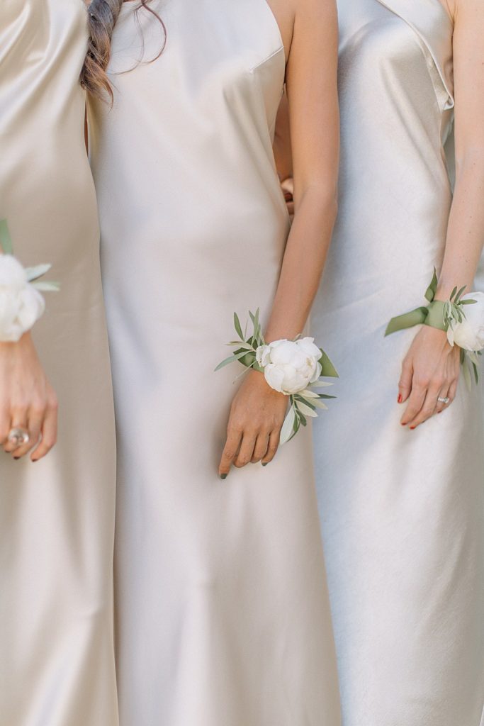 In questa foto le braccia di una sposa e le sue damigelle che indossano un corsage con peonia bianca e foglie di ulivo
