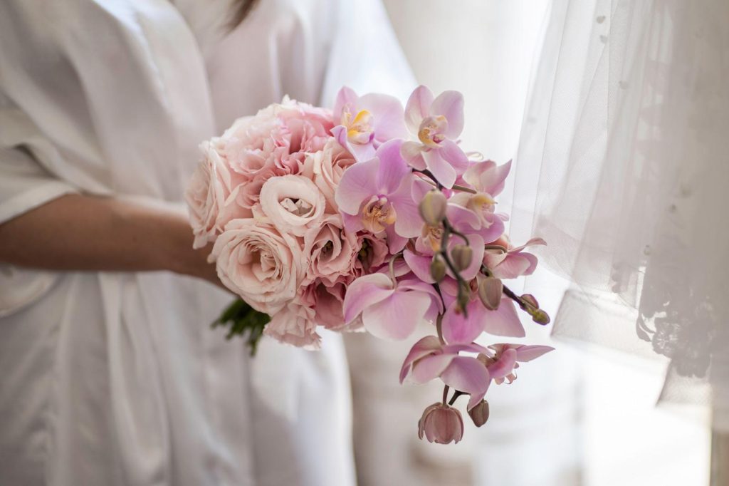 In questa foto una sposa in kimono bianco tiene tra le mani un bouquet di rose e orchidee rosa