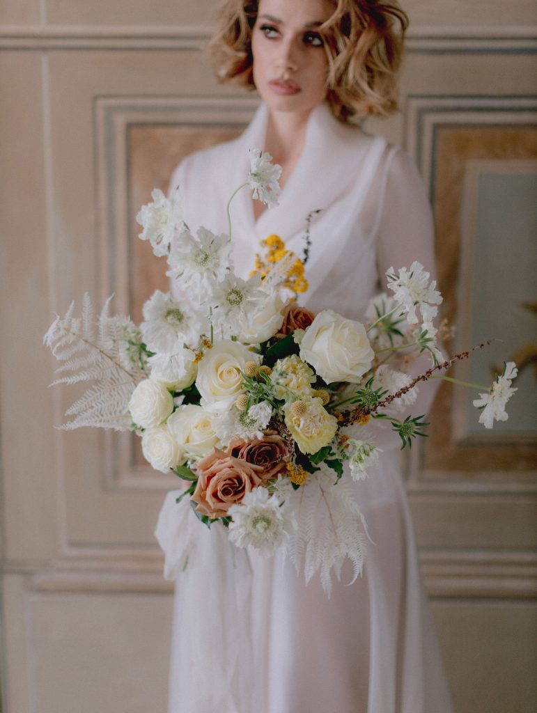 In questa foto una modella tiene tra le mani un bouquet di rose bianche, rose cappuccino, felci e margherite bianche 