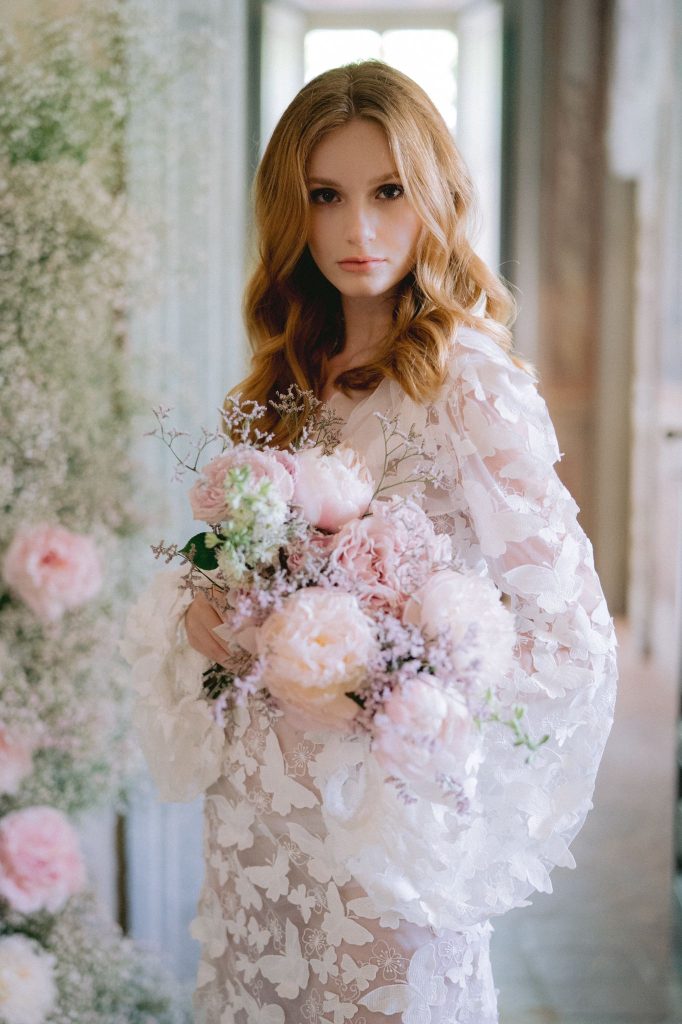 In questa foto una modella indossa un abito con mani balloon e farfalle 3d e tiene tra le braccia un bouquet di peonie rosa e gypsophila rosa 