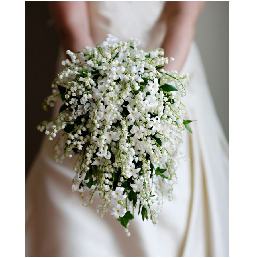 In questa foto le mani di una sposa che tengono un bouquet a cascata di mughetto