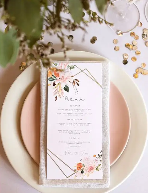 In questa foto un menù matrimonio in stile romantico nei toni del rosa con decori floreali poggiato sun un piatto rosa e su uno bianco