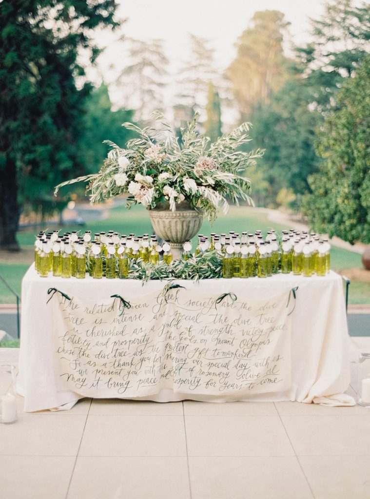 In questa foto un tavolo per bomboniere matrimonio con bottigliette di olio allestito nel giardino di una villa