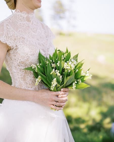 In questa foto, una sposa minimal tiene in mano un mini bouquet di mughetto bianco