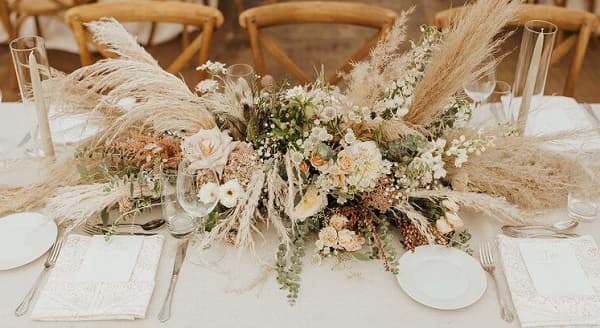 In questa foto, un centrotavola fiori matrimonio Boho chic realizzato con rose e fiori dai toni neutri ed erba della Pampas 