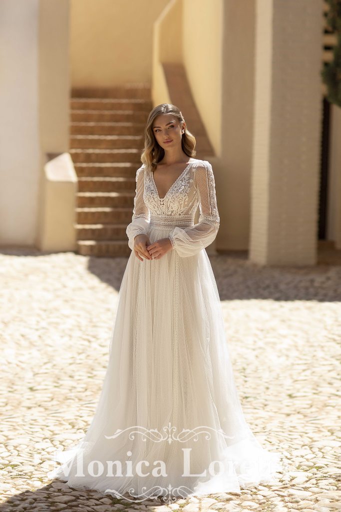 In questa immagine un abito da sposa Monica Loretti 2023 con maniche lunghe in tulle e ricami in pizzo