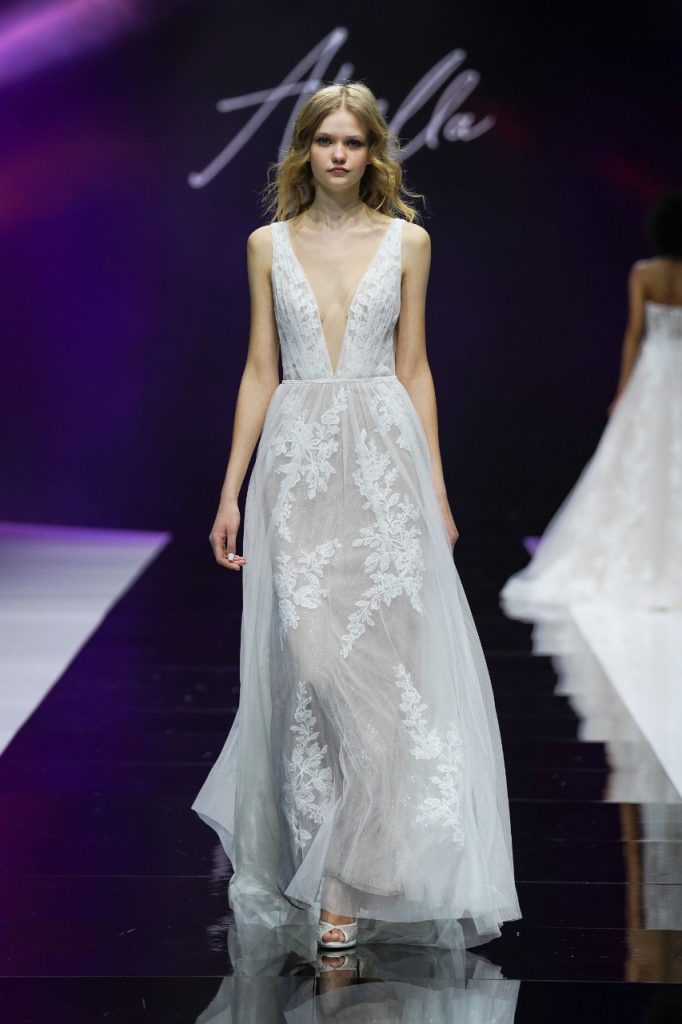 In questa foto la modella indossa un abito da sposa Allure Bridals 2023 con profondo scollo a V e pizzo.