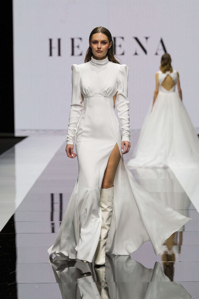 In questa foto la modella indossa un abito da sposa Helena 2023 con con maniche lunghe e spacco davanti.