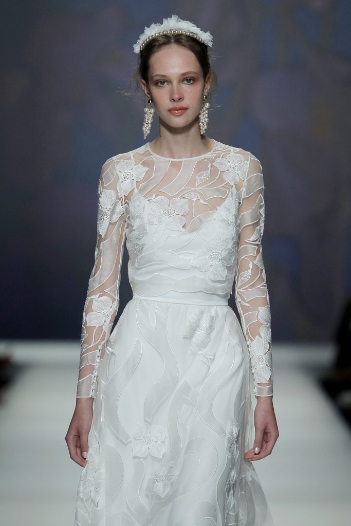 In questa foto una modella indossa un abito da sposa bianco con patten floreale e trasparenze.