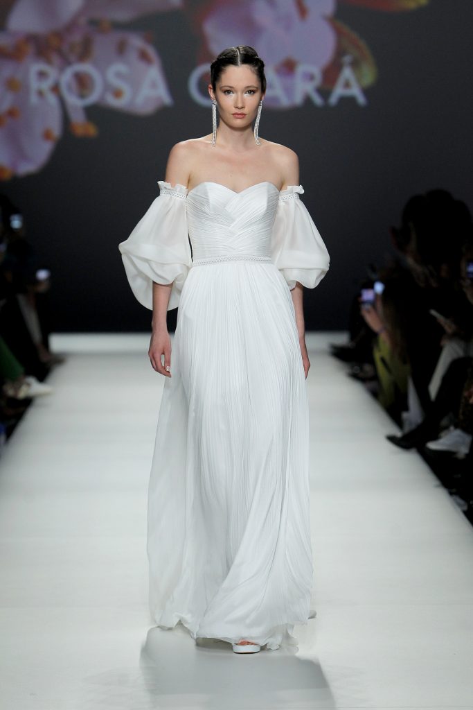 In questa foto la modella indossa un abito da sposa scivolato 2023 con corsetto e maniche balloon Rosa Clarà