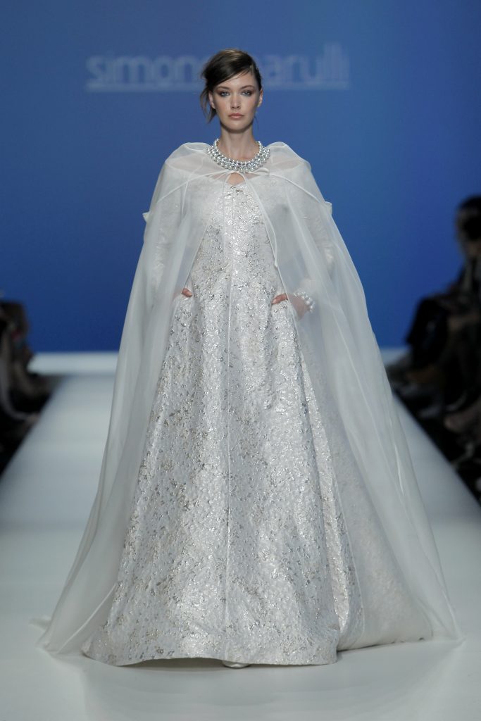 In questa foto la modella indossa un abito bianco e argento con mantella trasparente di Simone Marulli.