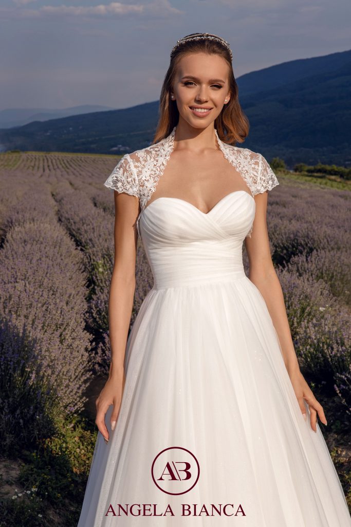 In questa foto una modella indossa un abito da sposa in chiffon con scollatura a cuore un coprispalle da sposa in pizzo a maniche corte