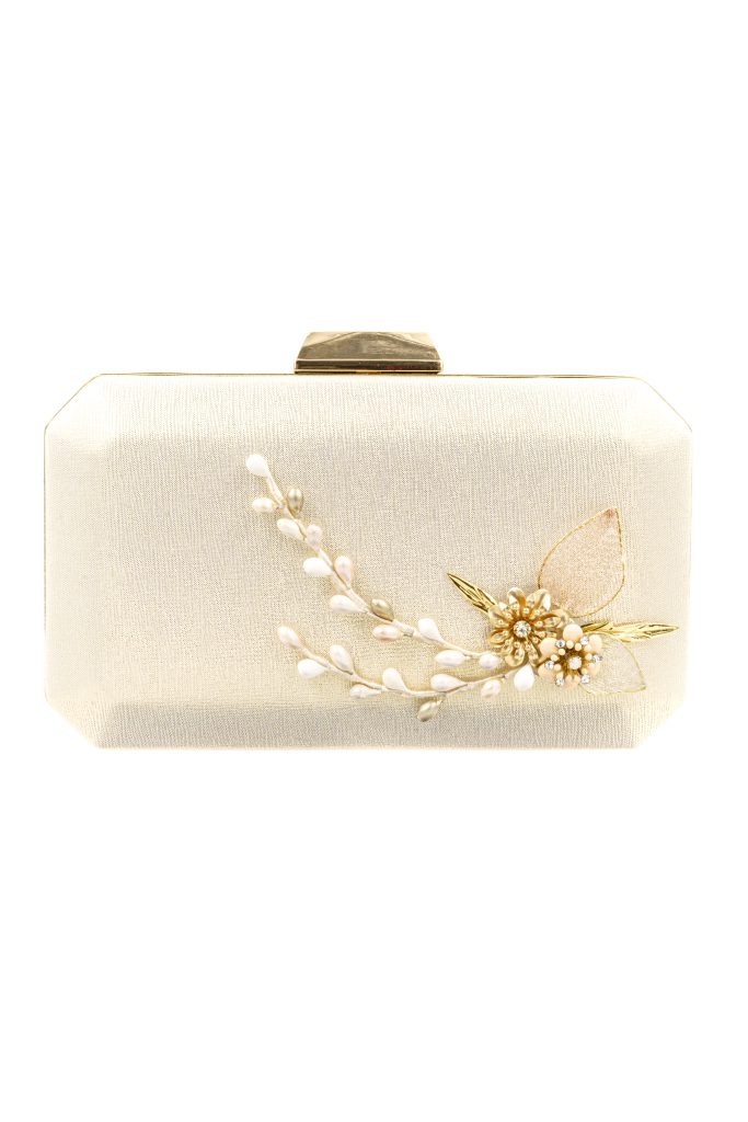 In questa foto una borsa da sposa di Higar Novias modello clutch di colore bianco con chiusyra colore oro e dettagli gioiello a forma di fiore sulla parte anteriore con perline e cristalli