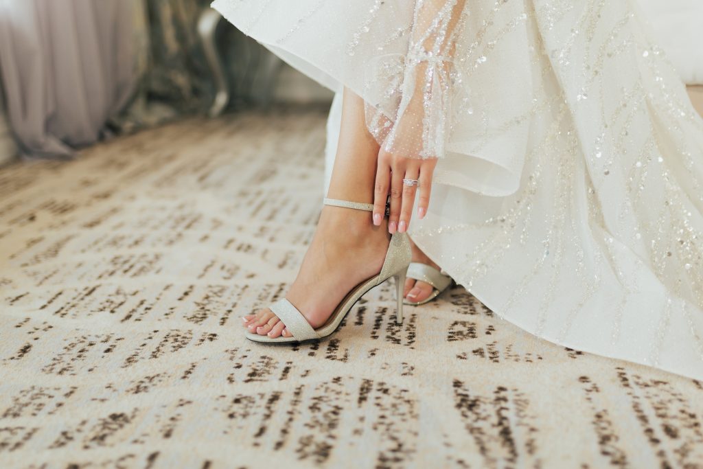 In questa foto i piedi di una sposa mentre chiude il cinturino del suo sandalo bianco con tacco basso