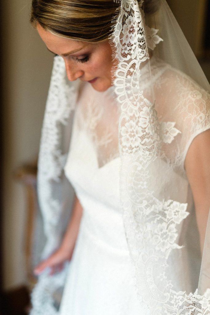 In questa foto una sposa indossa un velo a mantiglia con bordo in pizzo di Giuliani Couture