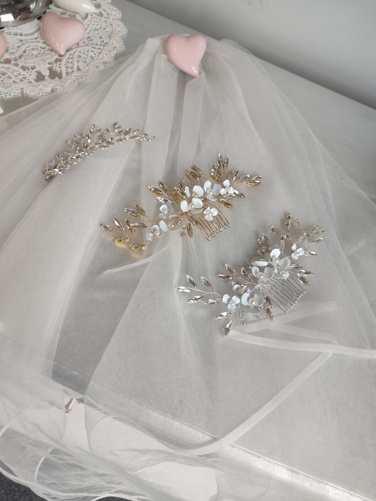 In questa foto 3 fermagli per capelli da sposa di Annais Bridal. Il primo fermaglio in alto presenta cristalli trasparenti, il secondo è colore oro e presenta cristalli e fiori di colore bianco in porcellana, il terzo è di colore argento con cristalli e fiori bianchi di portacellana