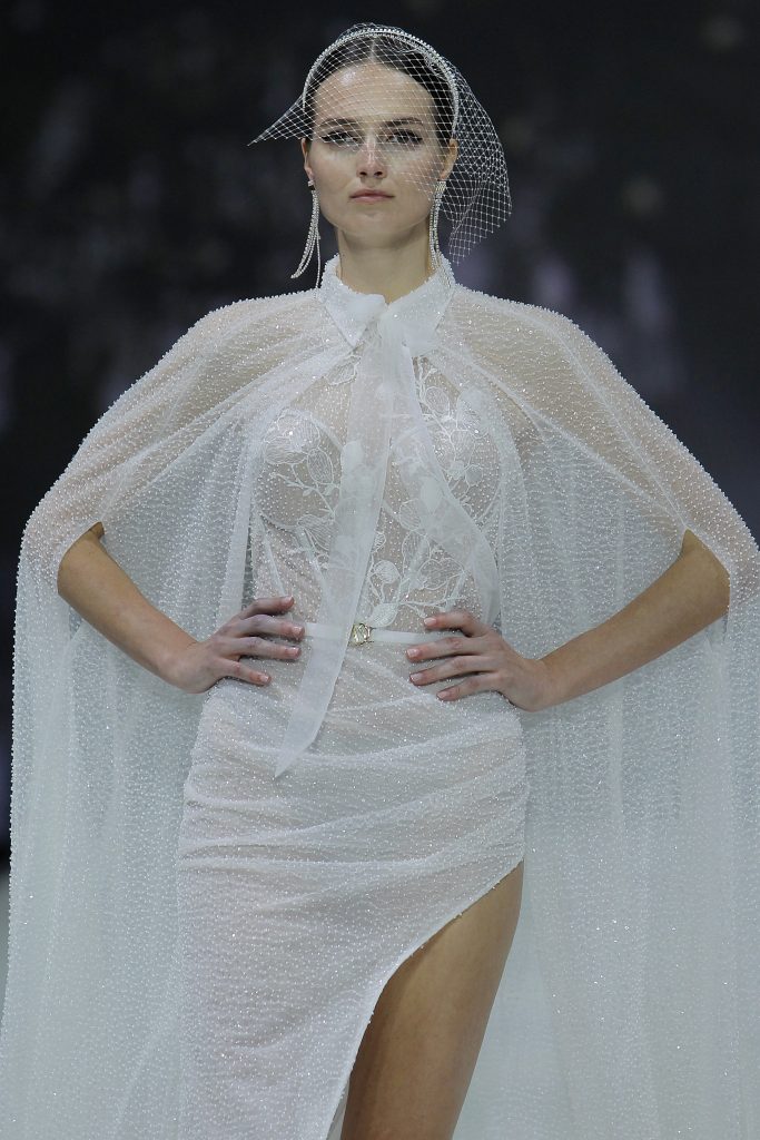 In questa foto la modella indossa un abito da sposa corto con mantella e trasparenze.