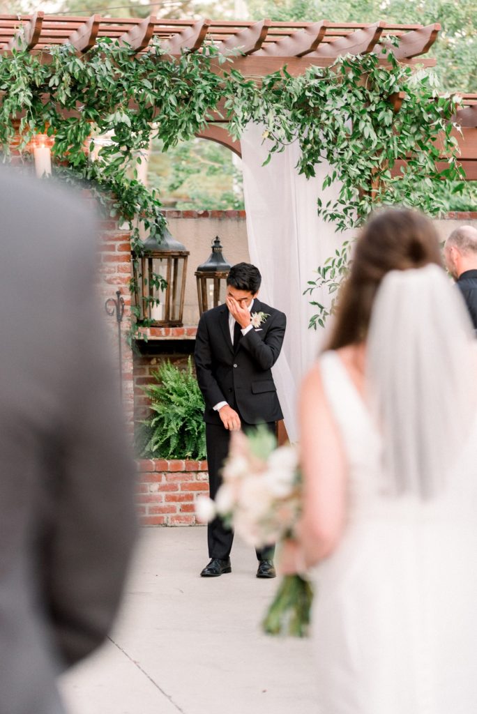 In questa foto uno sposo all'altare di un matrimonio civile si commuove all'ingresso della sposa. Lo sposo è a fuoco, la sposa è sfocata sulla destra