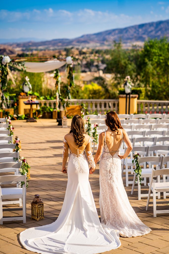 In questa foto l'ingresso di due spose in un matrimonio gay. Le due spose indossano un abito a semisirena con lungo strascico