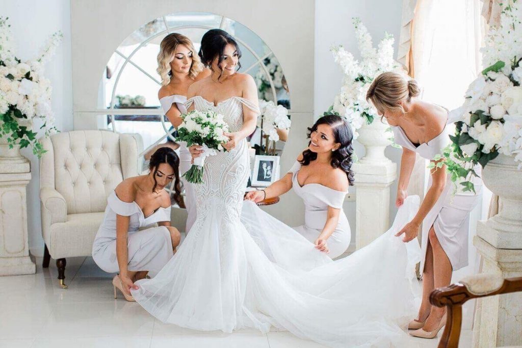 In questa foto una sposa che guarda le sue damigelle mentre le sistemano lo strascico del suo abito
