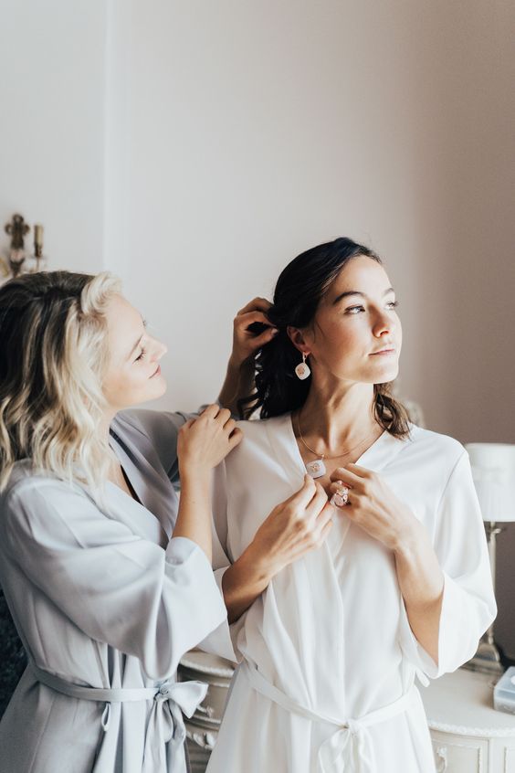 In questa foto la preparazione della sposa mentre la damigella la aiuta ad indossare i suoi orecchini spostandole i capelli dal viso