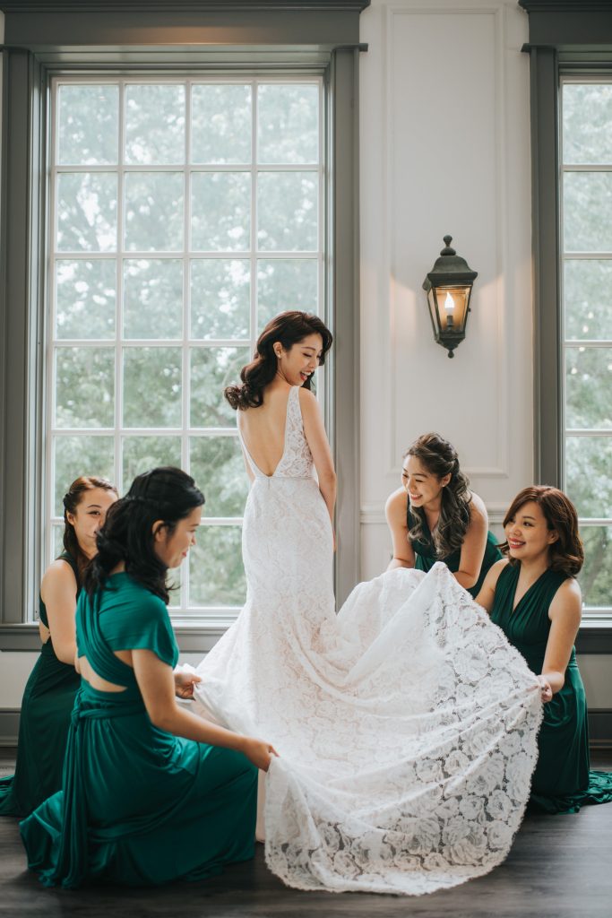 In questa foto le damigelle della sposa vestite con un abito colore verde bosco le distendono lo strascico in pizzo rebrodé mentre lei girata le guarda sorridendo