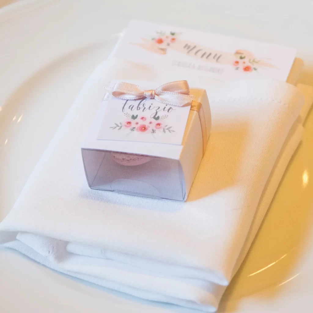 In questa foto segnaposto matrimonio  portaconfetti con tag e nastro colore rosa. Sotto il nome dell'ospite sono disegnati piccoli fiori abbinati