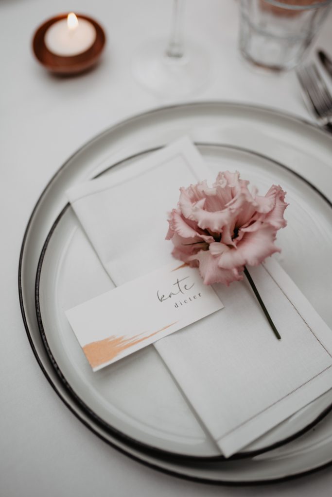 In questa foto un segnaposto per matrimonio con biglietto colore bianco sotto ad un fiore colore rosa