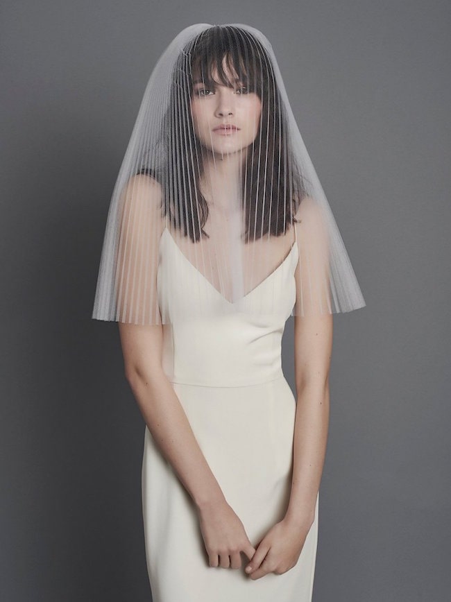 In questa foto una modella indossa un  abito bianco effetto lingerie e un velo da sposa a triangolo in tulle plissè