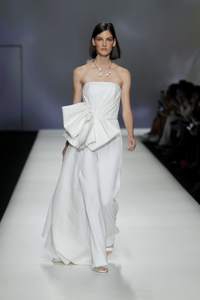 In questa foto la modella indossa un abito da sposa con pantaloni e maxi fiocco Isabel Sanchis 2023.