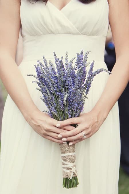 In questa foto, una sposa tiene in mano un semplice ed elegante bouquet di lavanda