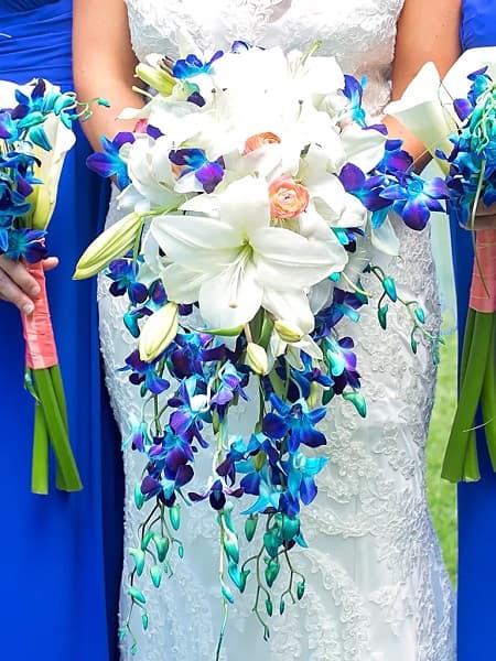 In questa foto, una sposa tiene in mano un bouquet a cascata realizzato con fiori bianchi e blu