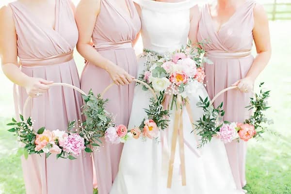 In questa foto, una sposa tiene in mano un bouquet sui toni del rosa, riproposto in quelli a hula hoop delle tre damigelle per fiori matrimonio rosa