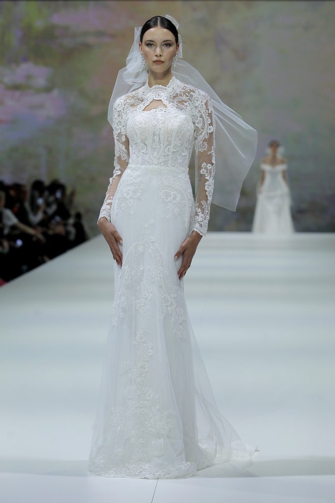 In questa foto la modella indossa un abito da sposa aderente con maniche di pizzo Marchesa for Pronovias 2023.