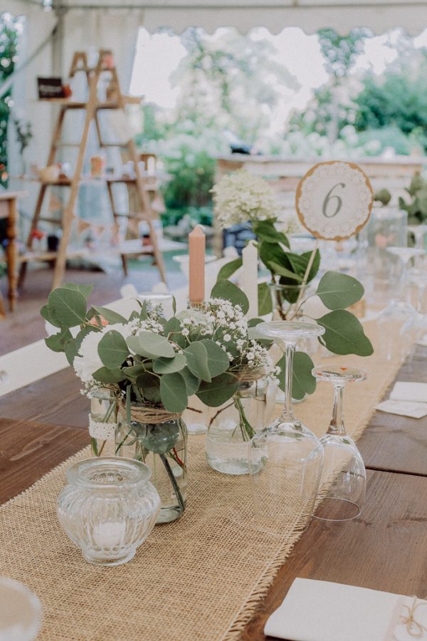 In questa foto addobbi per tavoli in stile Country Chi con vasetti di eucalipto e fiori bianchi su runner di juta