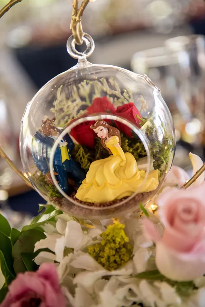 In questa foto una decorazione per tavolo a tema Disney con una sfera trasparente con Belle della Bella e la Bestia