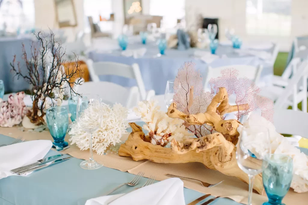 In questa foto addobbi per tavoli a tema mare con tovagliato colore azzurro polvere, bicchieri colore blu, legni e conchiglie