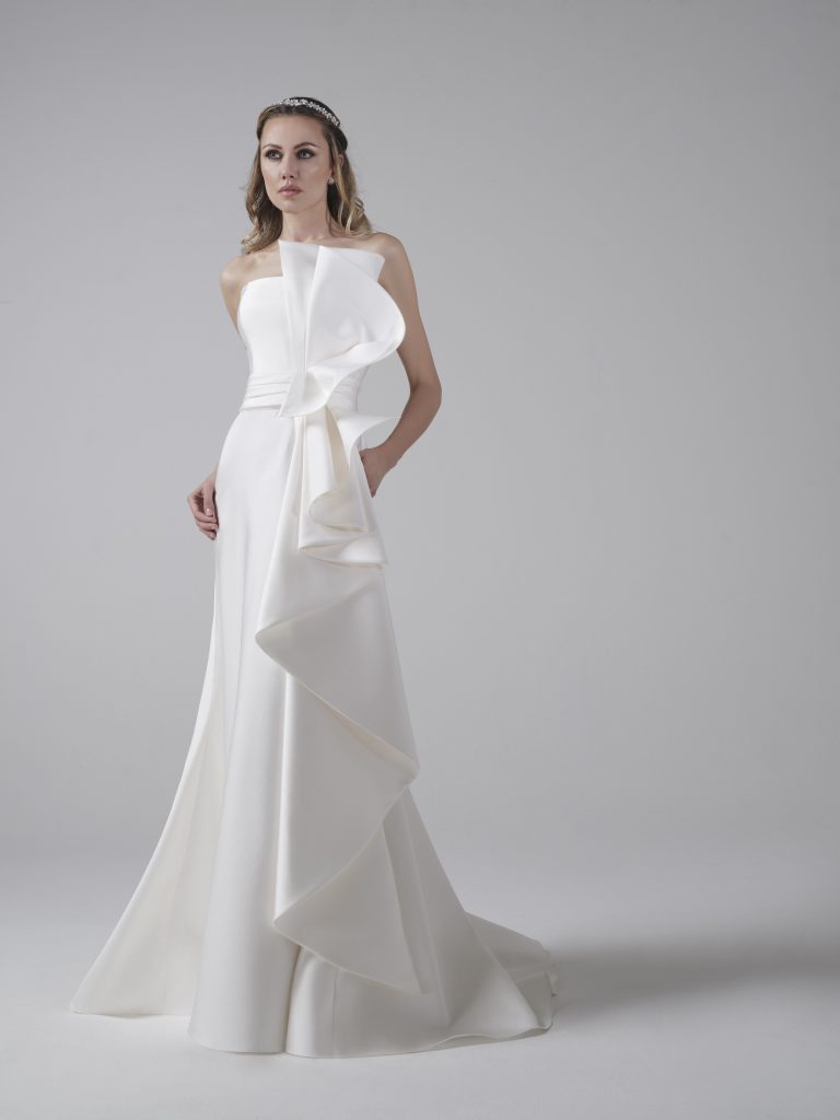 In questa foto una modella indossa un abito da sposa a semisirena in bianco ottico della collezione Musa Bridal di Maison Mirage perfetto