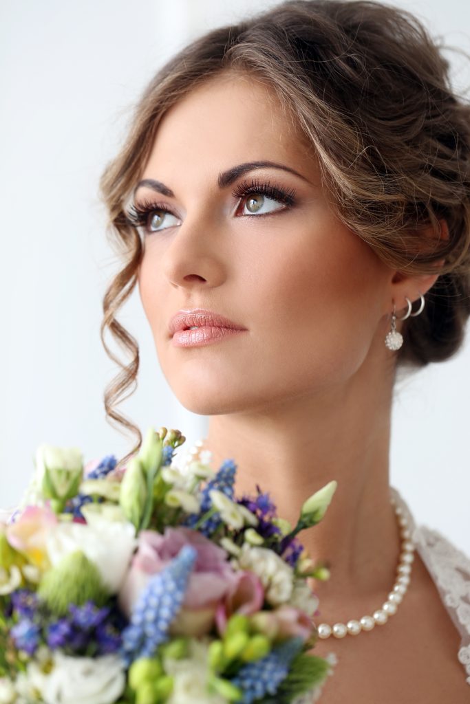 In questa foto un sposa con trucco realizzato secondo l'armocromia sposa. In primo piano è mostrato il suo bouquet di rose colore lilla e fiori di colore viola e bianco