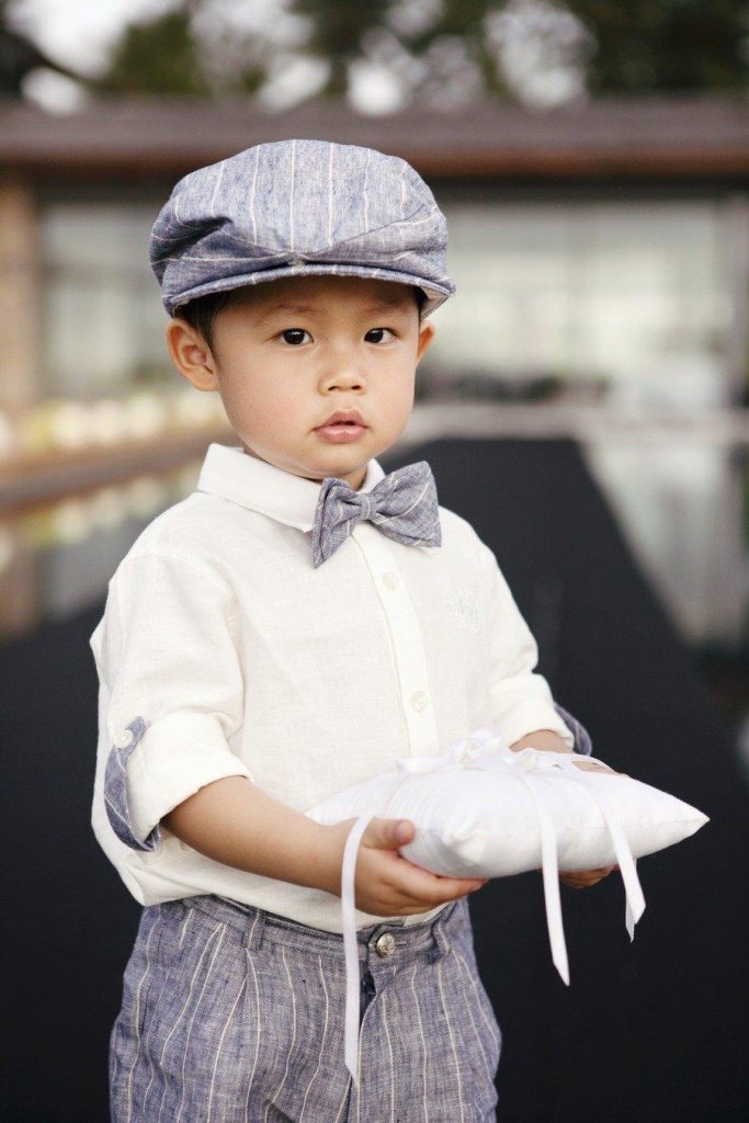 In questa foto un paggetto tiene in mano un cuscino portafedi. Il bimbo indossa una camicia bianca con bermuda colore carta da zucchero a righe e un papillon e una coppola abbinati