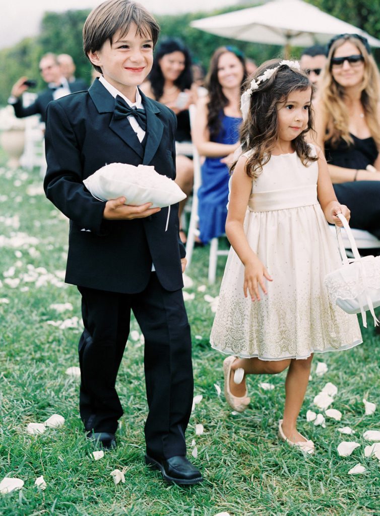 In questa foto un paggetto portafedi e una damigella lancia petali fanno il loro ingresso lungo un navata creata in un giardino per un matrimonio civile