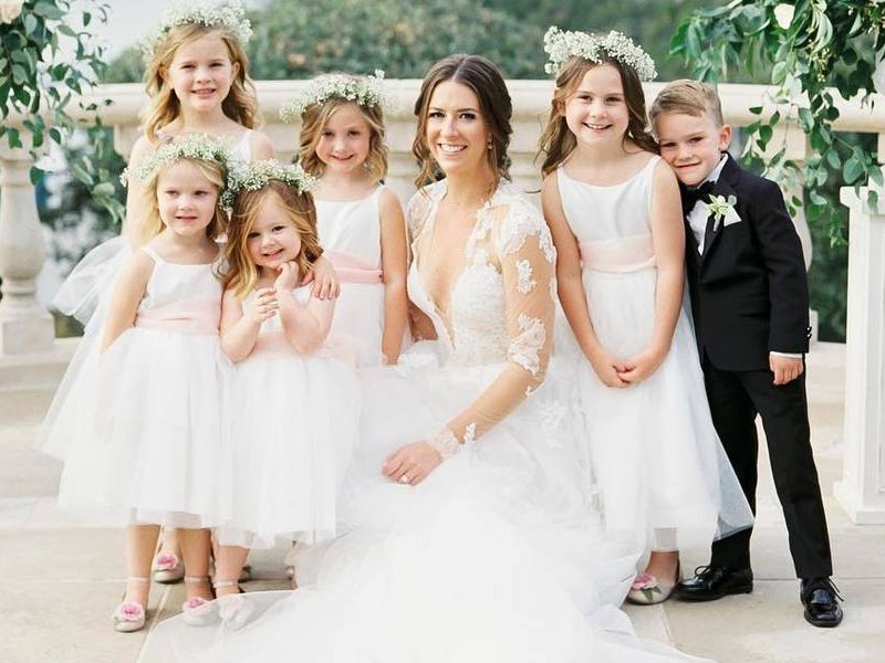 In questa foto una sposa sorridente posa con damigelle e paggetti del suo matrimonio