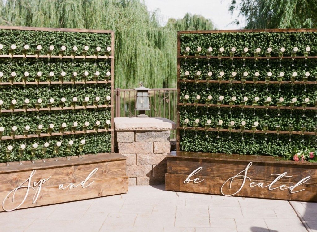 In questa foto escort card su flute con prosecco disposti su due pannelli di legno decorati con foglie