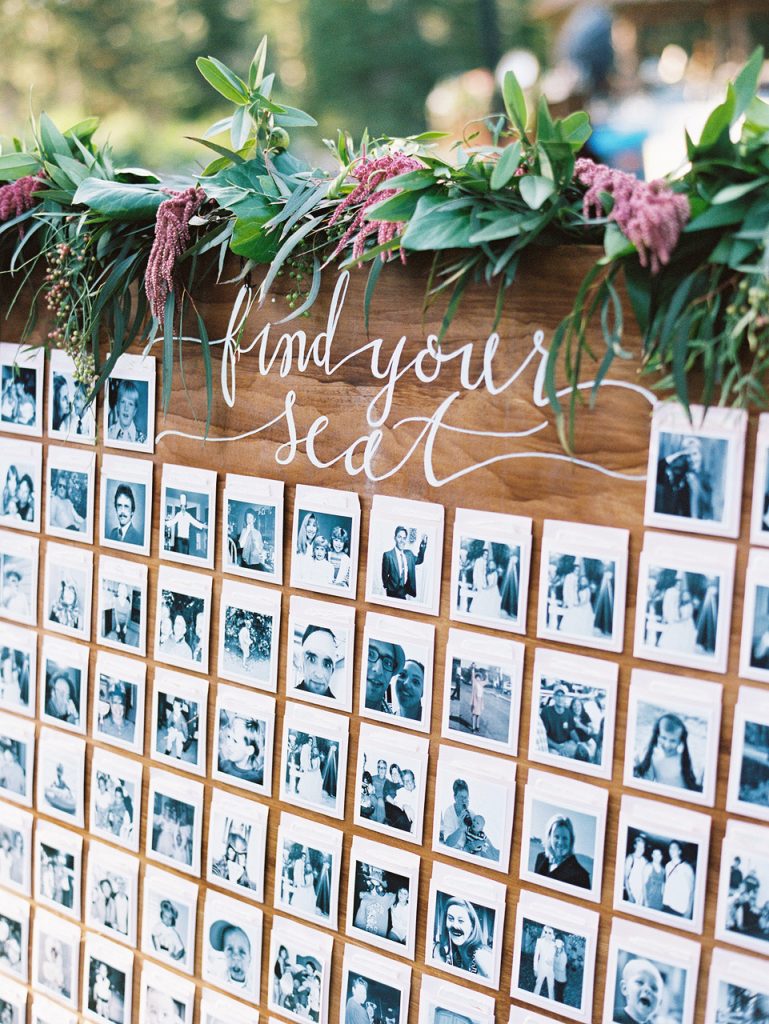 In questa foto un tableau di nozze originale creato con le foto formato Polaroid di tutti gli invitati disposte su una tavola di legno e decorata con foglie e fiori rosa 